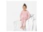 Une fille porte un pyjama rose à motifs cœurs sur un lit.