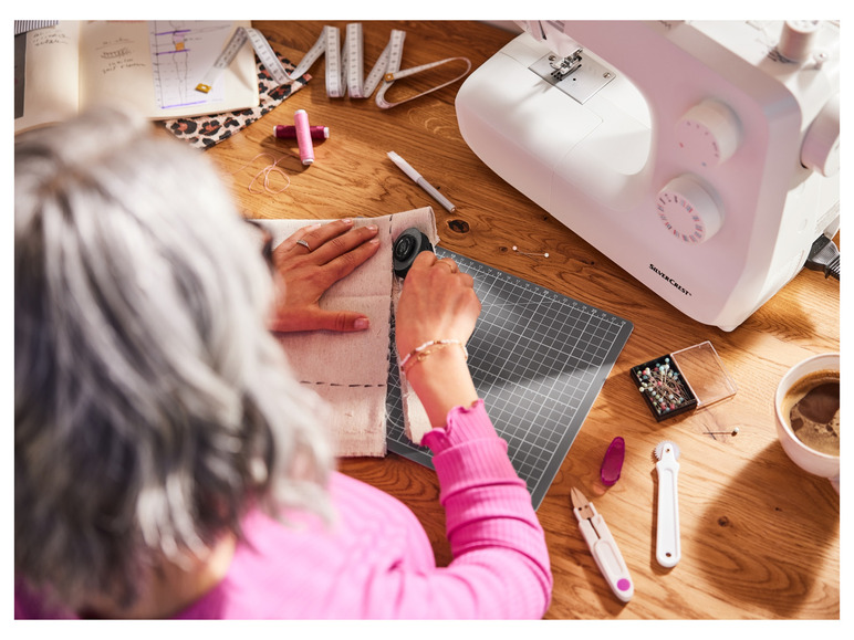 Une femme travaillant avec un couteau rotatif sur du tissu, avec une machine à coudre et d'autres accessoires de couture à côté