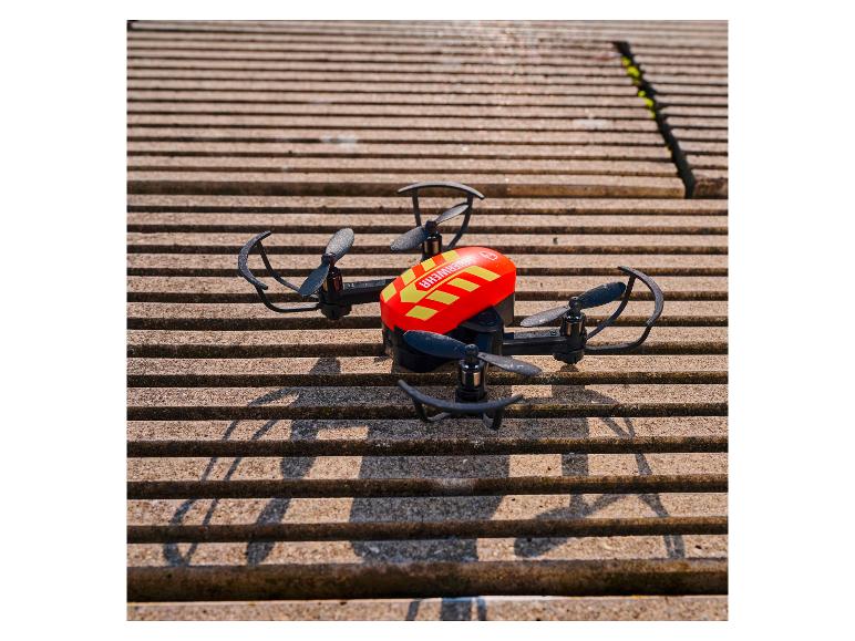 Drone rouge et noir avec hélices sur une surface en béton rayée.