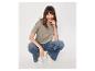 Femme en t-shirt kaki, jean large et baskets blanches, souriante.