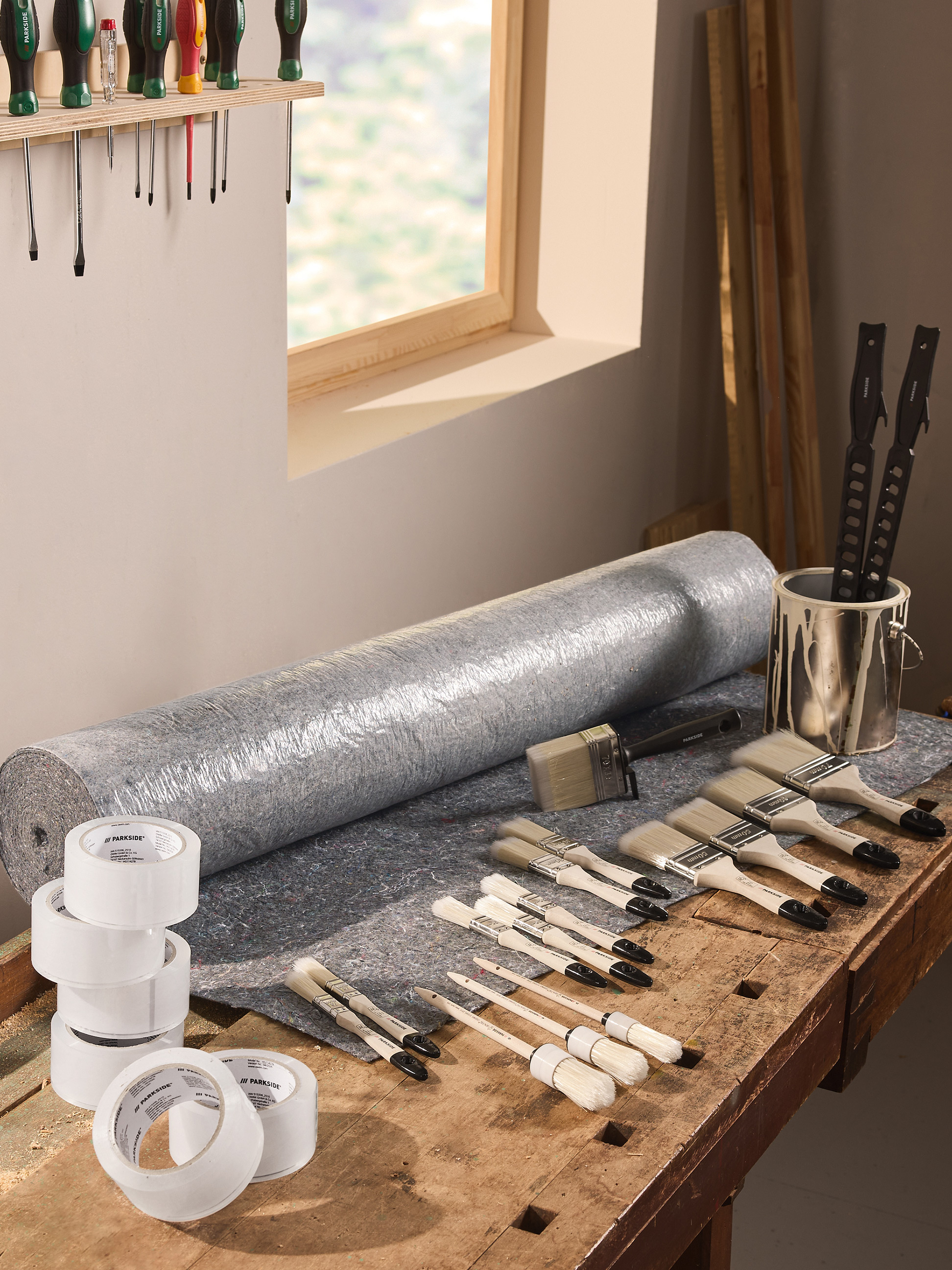 Outils et fournitures de peinture, y compris pinceaux, film de protection et ruban adhésif, sur un établi.