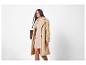 Femme en long manteau beige, robe en maille et bottes marron.