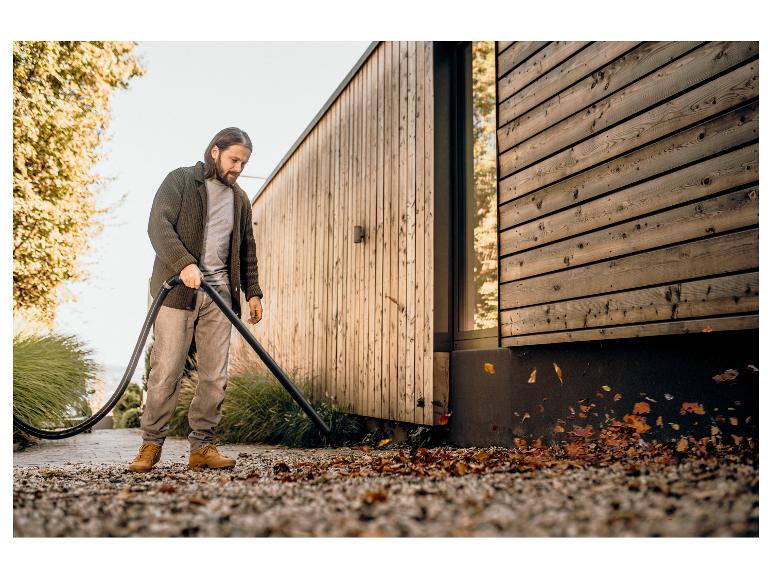 Homme avec souffleur de feuilles nettoyant près d'une maison en bois.