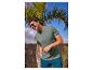 Homme en t-shirt vert avec 'Thrive in the unknown', short bleu et lunettes de soleil.