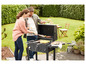 Un couple fait un barbecue dans le jardin avec un barbecue avec une grille et une table latérale.