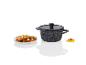 Une casserole noire avec un couvercle, à côté d'une assiette de légumes rôtis.