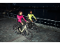 Deux personnes en vestes de cyclisme réfléchissantes à vélo électrique la nuit au bord d'une rivière.