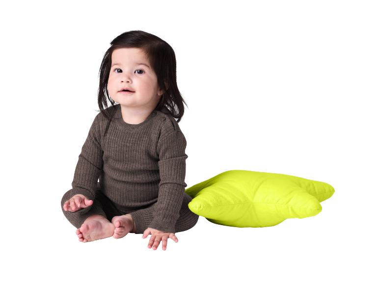 Bébé en grenouillère marron assis à côté d'un coussin vert vif.