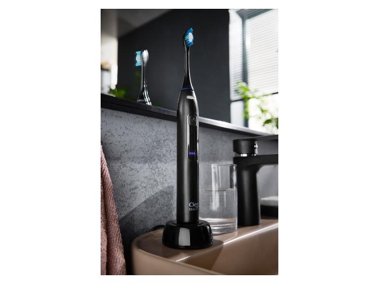 Brosse à dents électrique noire sur son chargeur à côté d'un lavabo de salle de bain.