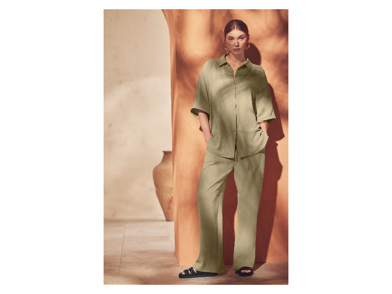 Une femme pose avec un ensemble pantalon et chemise vert clair et des sandales noires.