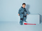 Un enfant dans une combinaison bleue avec un motif de vélo et des bottes bleues, assis sur une plate-forme avec une pelle rouge.