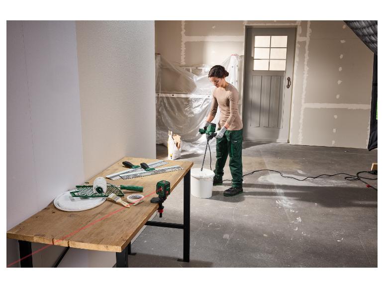 Femme mélangeant du plâtre avec un mélangeur, outils et niveau laser sur une table dans une pièce en rénovation.