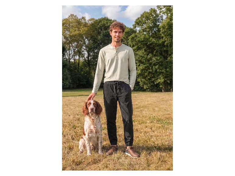 Homme en chemise à manches longues et pantalon caressant un chien à l'extérieur.