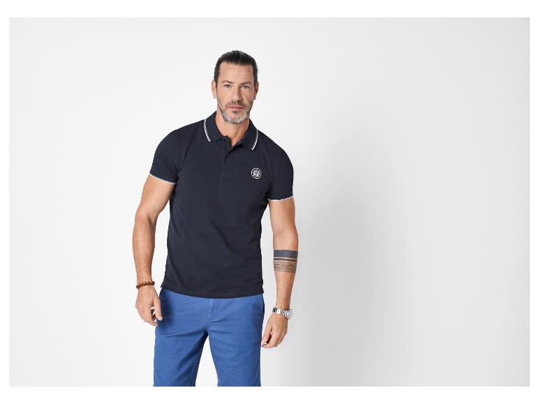 Homme en polo bleu marine à rayures blanches et short bleu.