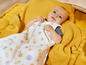 Un bébé dans une gigoteuse à motifs de fruits, allongé sur une couverture jaune.