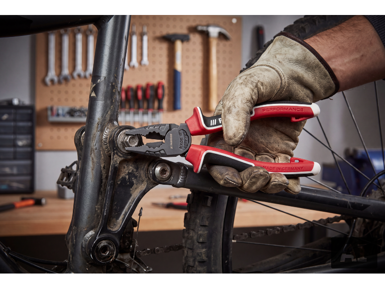 Une main gantée utilise une pince multiprise pour serrer un boulon sur un cadre de vélo.