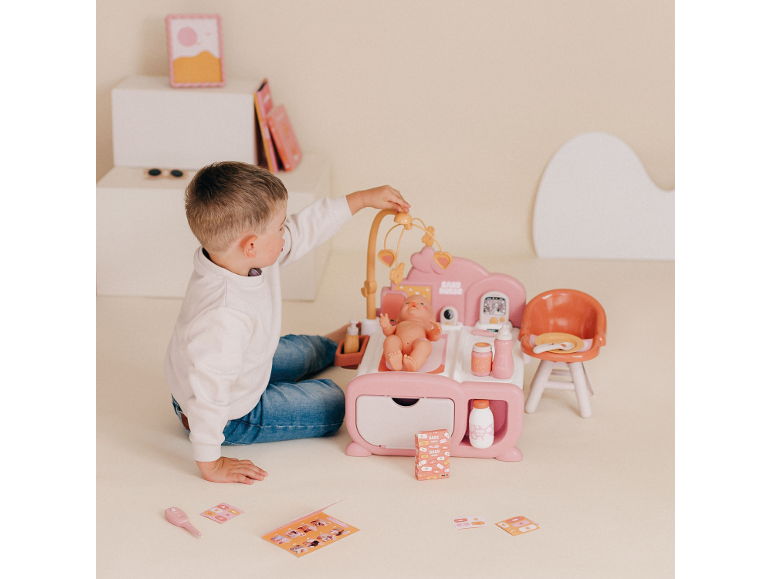 Garçon jouant avec une station de soins pour poupée rose avec bébé et accessoires.