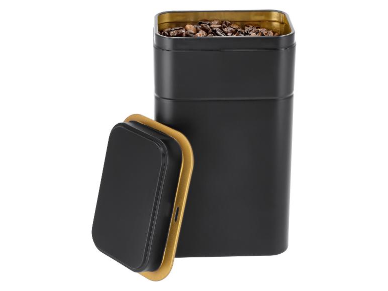 Boîte à café en métal noir avec intérieur doré et couvercle, remplie de grains de café.