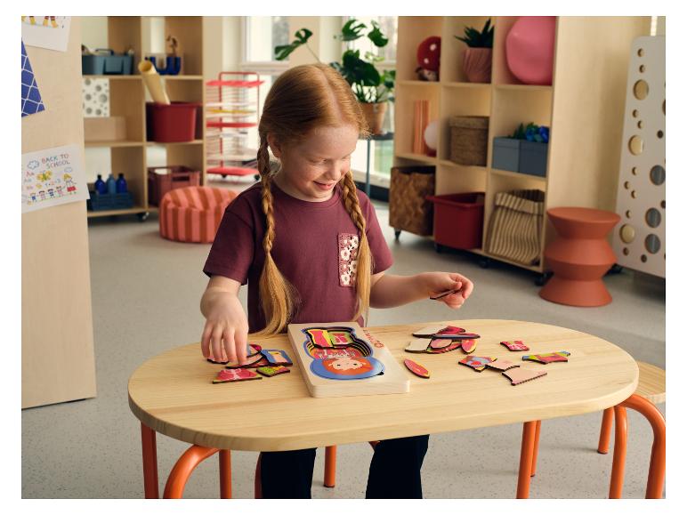 Une jeune fille jouant avec un puzzle en bois du corps humain LUPILU® sur une table.