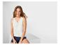 Femme en débardeur blanc en dentelle et short en jean assise sur un cube blanc.