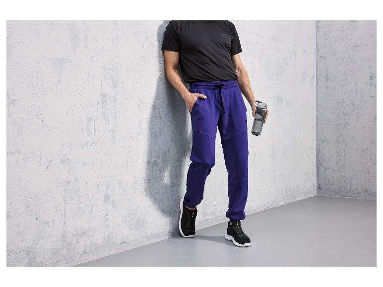 Homme portant un t-shirt noir et un pantalon de survêtement bleu avec une bouteille d'eau.