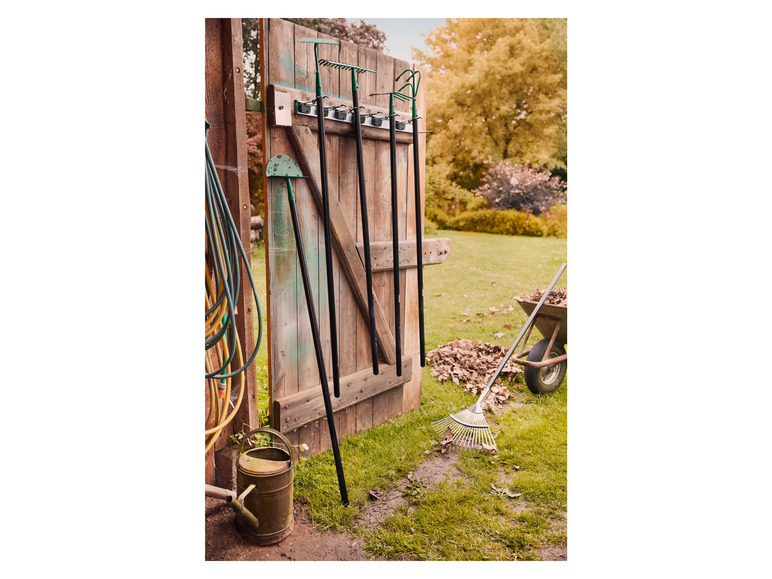 Des outils de jardinage, comme un râteau, une pelle et une binette, sont accrochés à une porte de grange en bois.