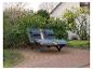 Chaise longue en bois avec coussins gris foncé sur une terrasse dans un jardin.