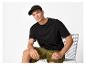 Homme en t-shirt noir, short olive et casquette noire, assis sur une chaise en métal.