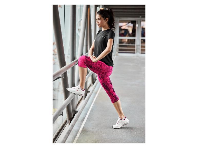 Femme en haut de sport noir, leggings roses et chaussures de course blanches.