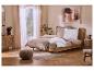 Chambre avec parure de lit beige à volants, lit et table de chevet en bois, et un tableau.