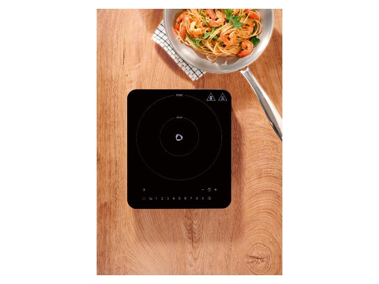 Table de cuisson à induction avec une poêle de pâtes aux crevettes sur une surface en bois.