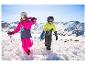 Deux enfants en combinaisons de ski, casques et lunettes marchant dans la neige avec des skis et des bâtons.