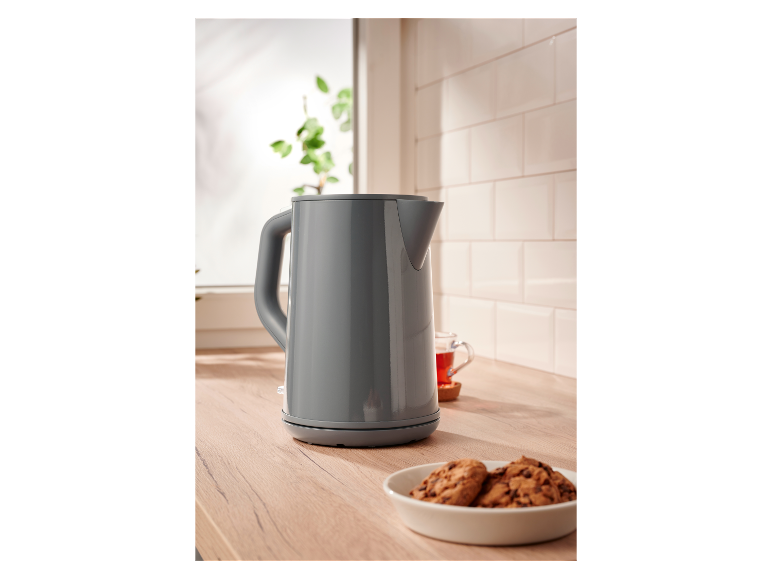 Une bouilloire grise sur un comptoir en bois à côté de biscuits.