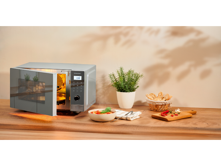 Micro-ondes argenté avec porte ouverte sur un plan de travail en bois à côté d'un bol de soupe