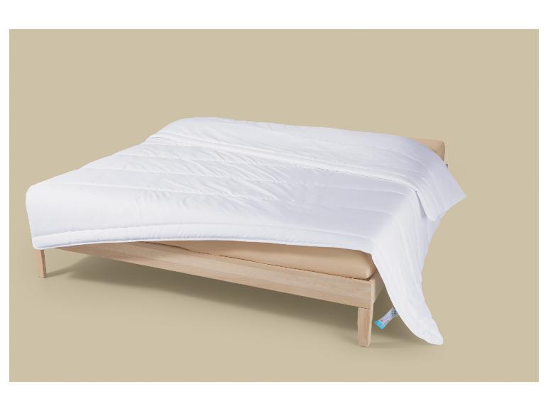 Couette blanche sur un lit en bois, avec une étiquette bleue visible.