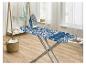 Table à repasser avec motif feuilles bleues, fer à repasser, étendoir avec chemises blanches et bleues et panier à linge.