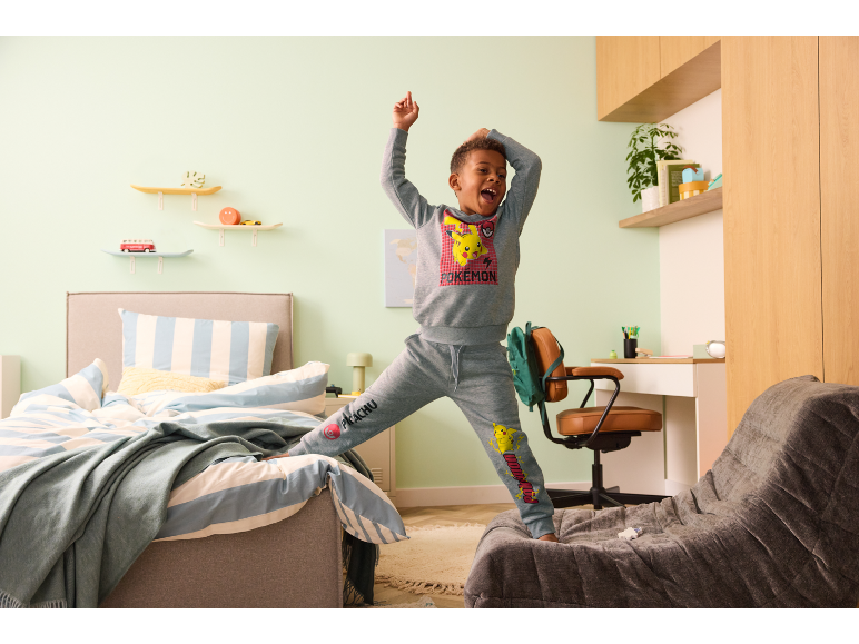 Garçon en ensemble de sport gris pour enfants avec motif de dessin animé posant dans sa chambre.