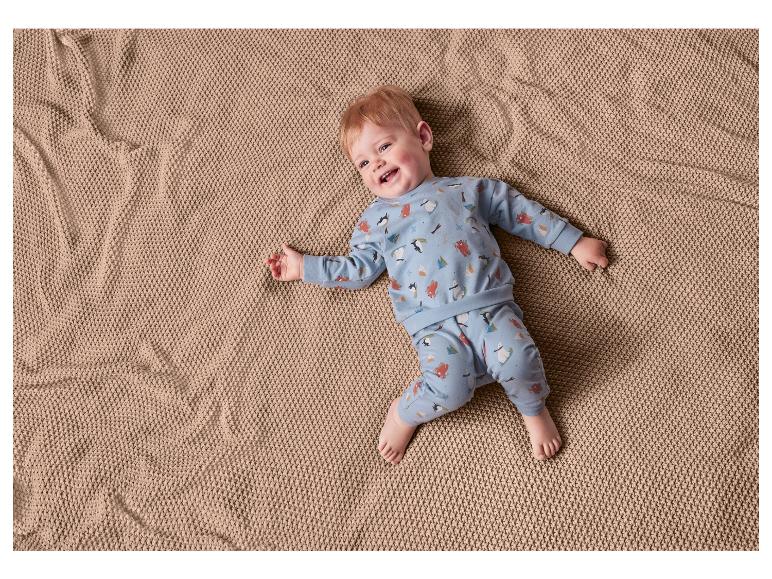 Bébé en pyjama bleu avec des pingouins et des ours sur une couverture marron.