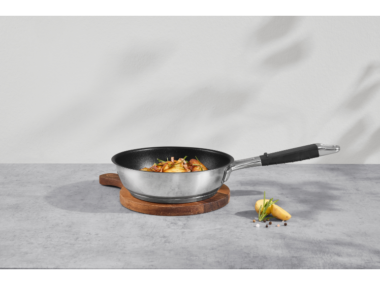 Poêle avec pommes de terre sautées et romarin sur une planche à découper en bois.