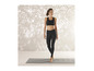 Une femme en leggings et soutien-gorge de sport noirs se tient sur un tapis de yoga.