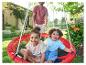 Deux enfants sourient dans une balançoire de jardin rouge, avec papa en arrière-plan.