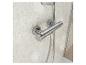 Un mitigeur thermostatique de douche chromé avec un flexible, monté sur un mur de salle de bain en carrelage.