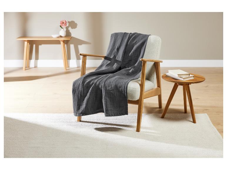 Une couverture en laine grise sur un fauteuil en bois avec une table basse en bois.