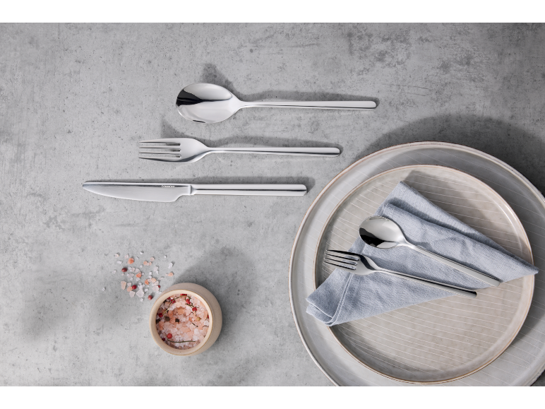 Ensemble de couverts avec assiettes, serviette et un bol de sel rose sur une surface grise.