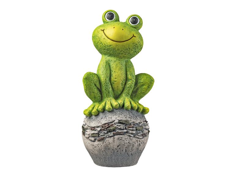 Une figurine de grenouille verte assise sur une boule de pierre.