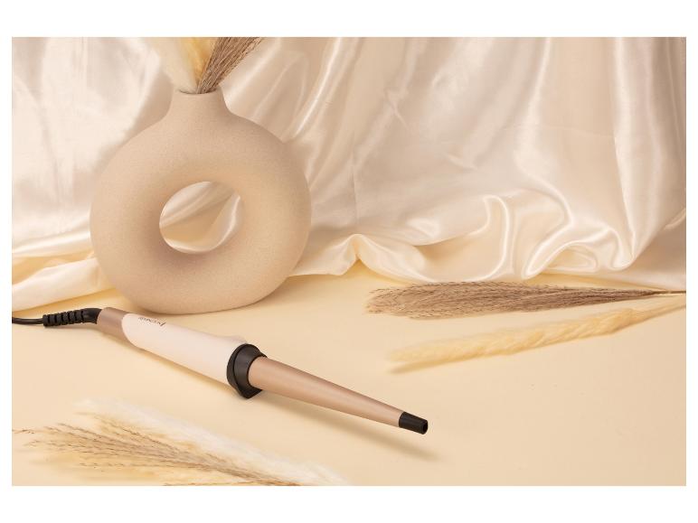 Fer à boucler sur fond beige avec un vase décoratif et de l'herbe de la pampa séchée.