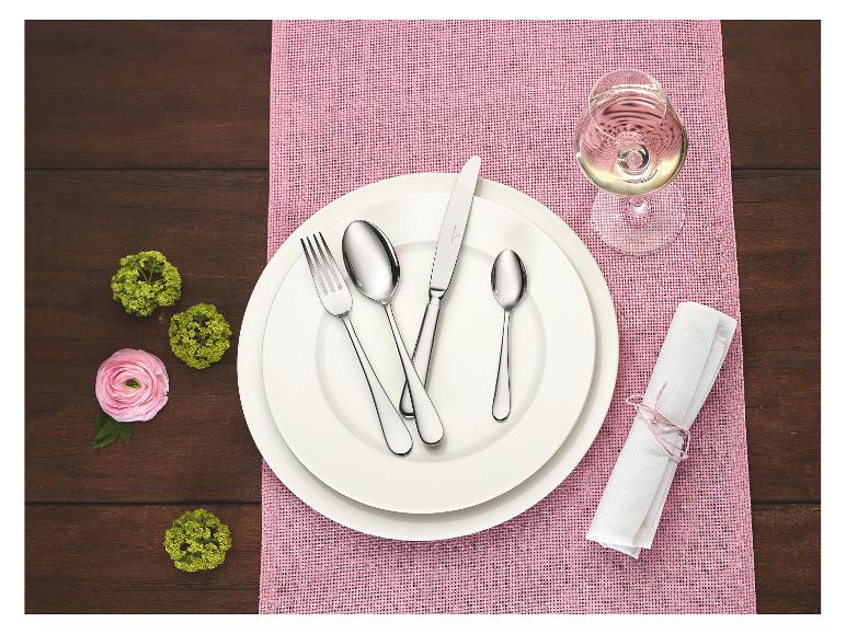 Table élégante avec assiettes blanches, couverts, un verre de vin blanc et des touches de rose.