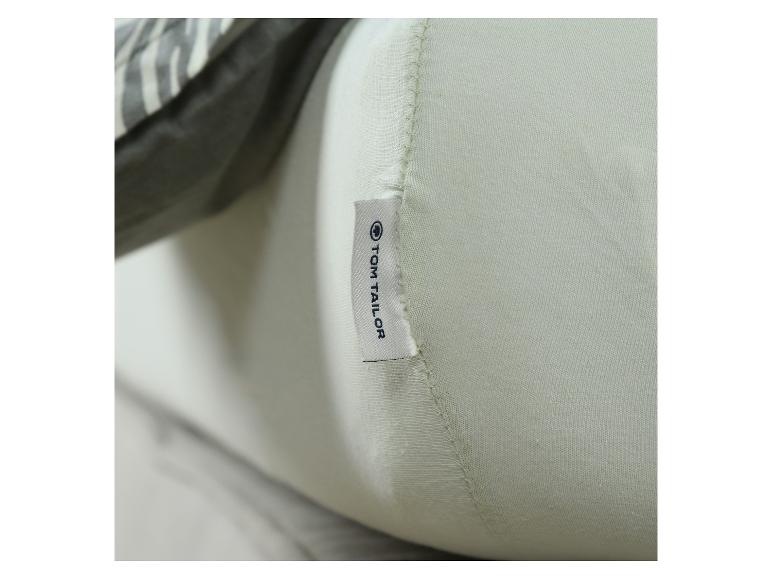 Oreiller vert clair avec une étiquette 'TOM TAILOR' et un tissu à motifs en arrière-plan.