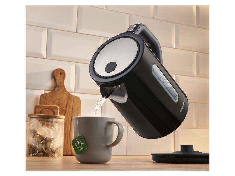 Bouilloire noire versant de l'eau chaude dans une tasse de thé avec un sachet de thé.
