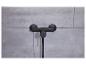 Un mitigeur de douche noir avec thermostat et pomme de douche, monté sur un mur de carreaux gris.